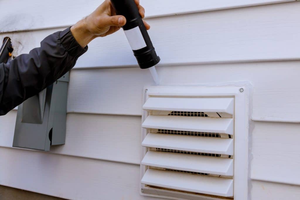 Dryer exhaust ventilation fan on side of house with plastic white trim with silicone